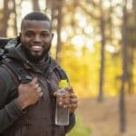 Happy guy with backpack smiling over forest background